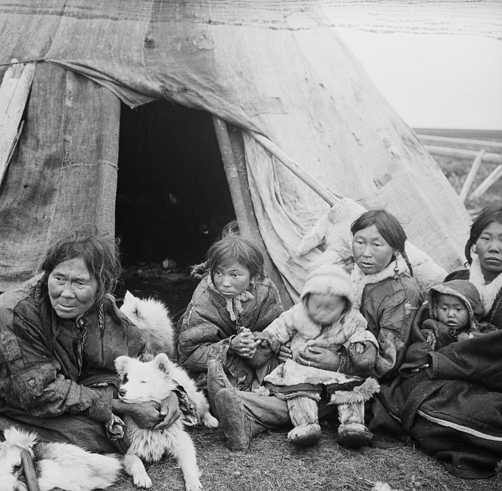 Mujeres y niños de la etnia nenet frente a la entrada de su tienda. Una de las mujeres lleva un perro alrededor del cuello. (Una de las fotos del viaje de Nansen a Siberia, del 2 de agosto al 26 de octubre de 1913). Ubicación: Rusia, Nosonovskiy Pesok. Biblioteca Nacional de Noruega